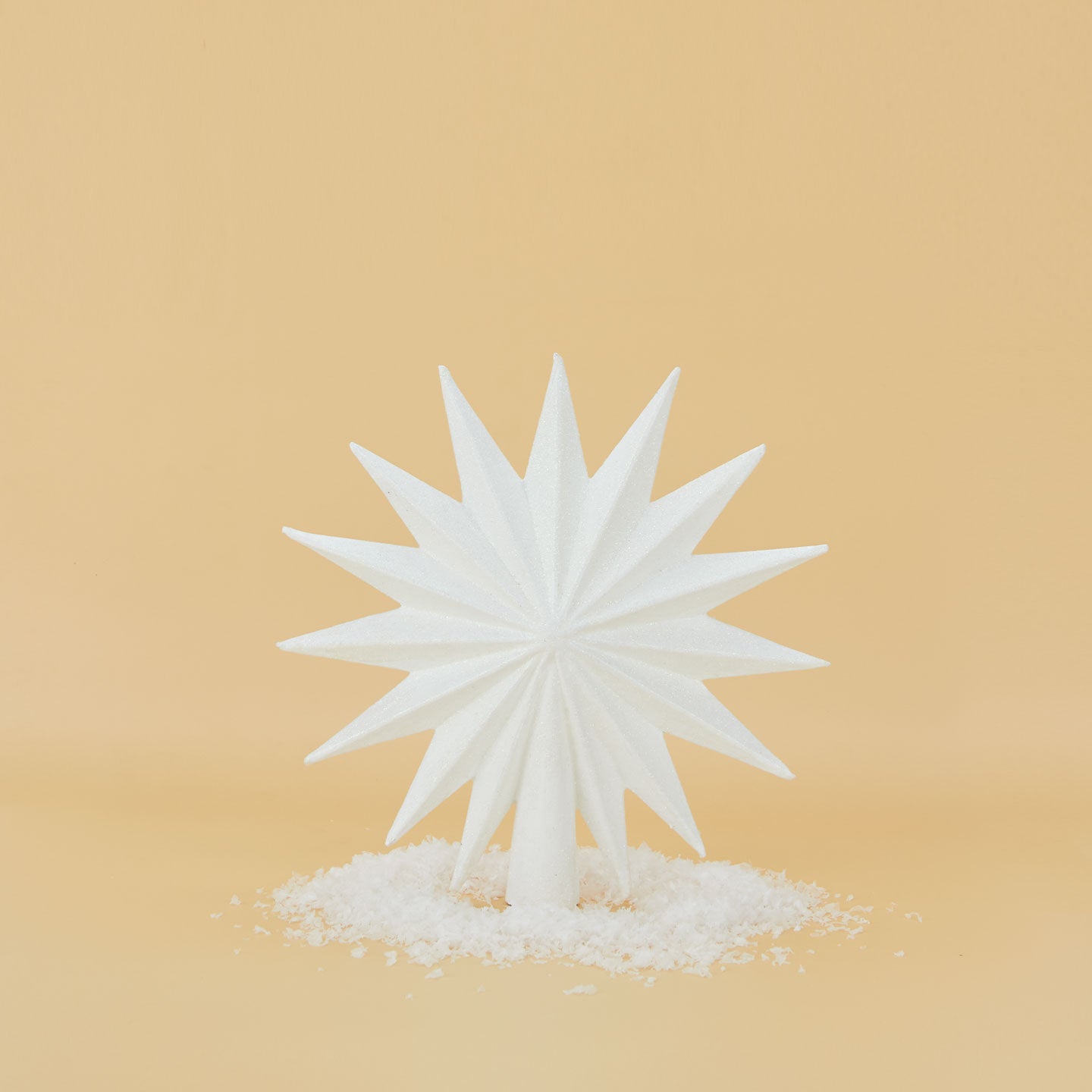 White 16 point star tree topper with snow around base.