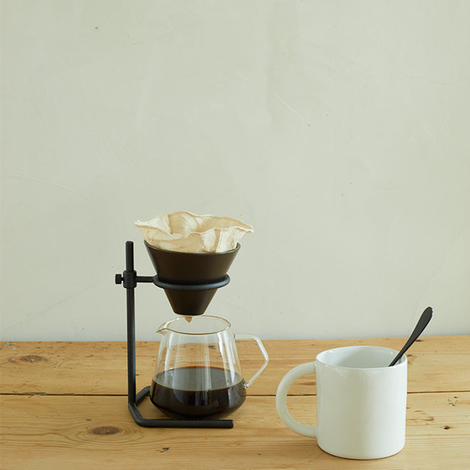 Coffee pourover stand, glass pitcher, mug and spoon on wooden countertop.