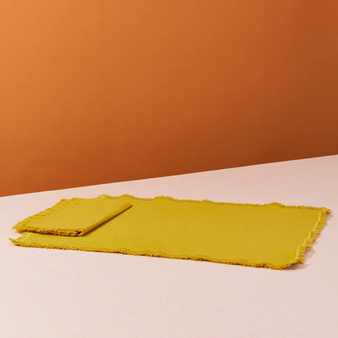 Mustard cotton placemats on pink surface. 