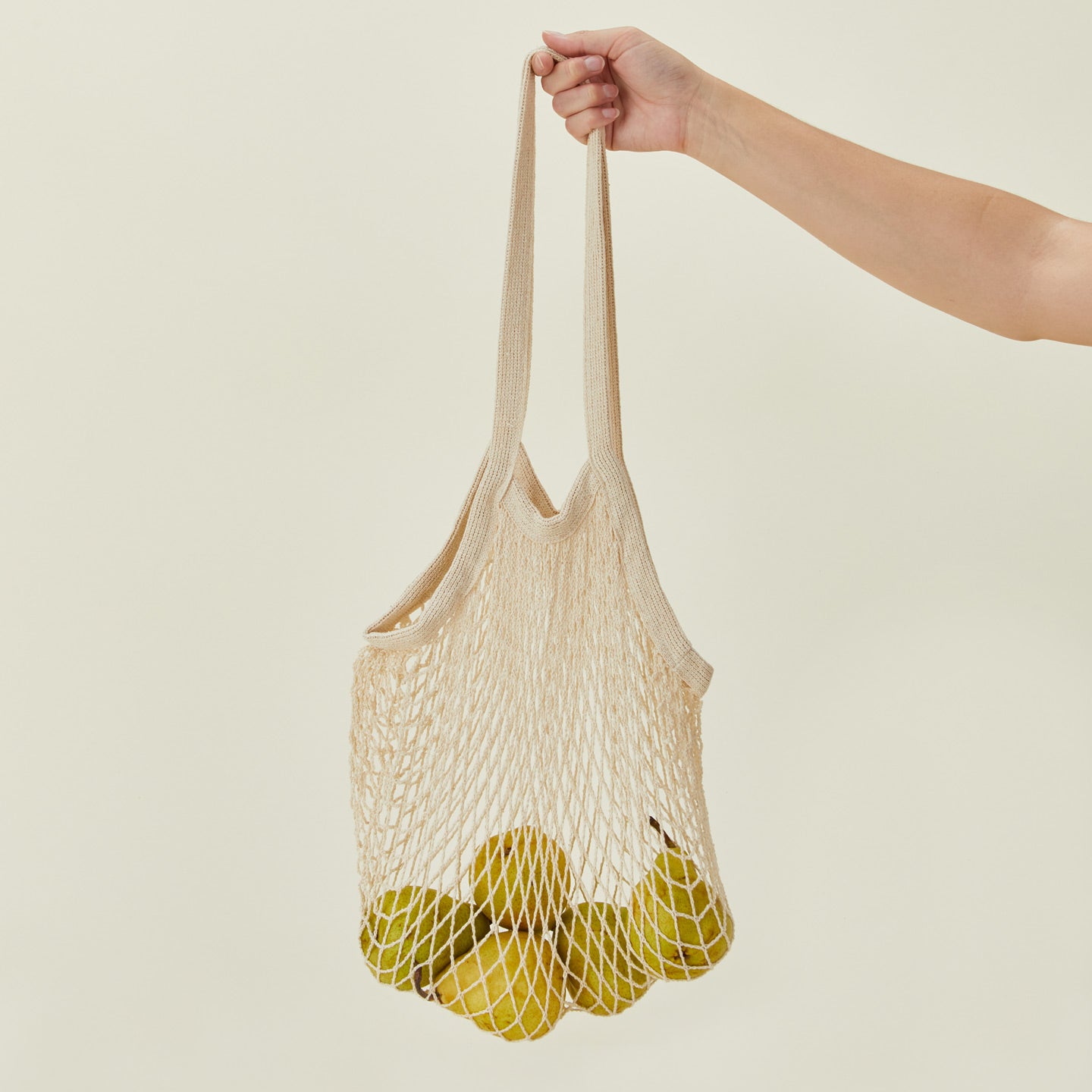 A Person carrying an Ecofreax reusable mesh cotton grocery bag filled with pears