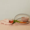 Glass of pink drink with carrots and a bowl on a pink surface