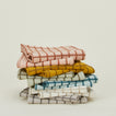 A stack of seven folded, checkered dish towels in various colors, including pink, yellow, green, blue, and white, against a light background.