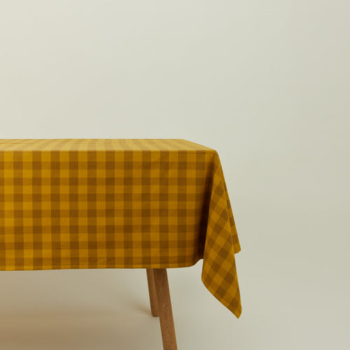 Essential Gingham tablecloth in mustard/bronze on a table.