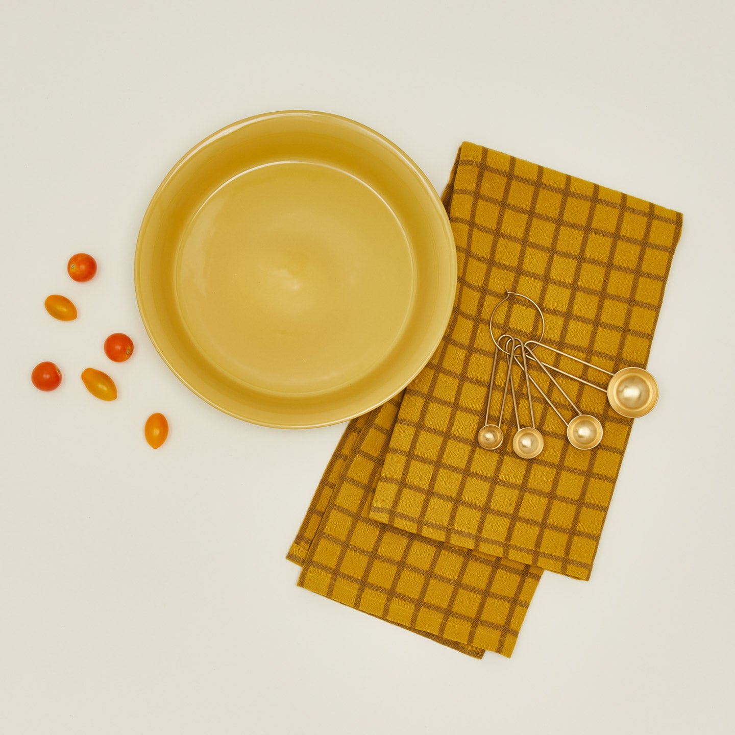 Essential pie dish in mustard with cherry tomatoes, measuring spoons, and dishtowel