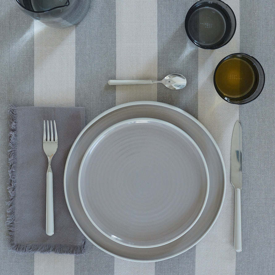Placesetting with Essential Dinner Napkin in Dark Grey on grey striped tablecloth.