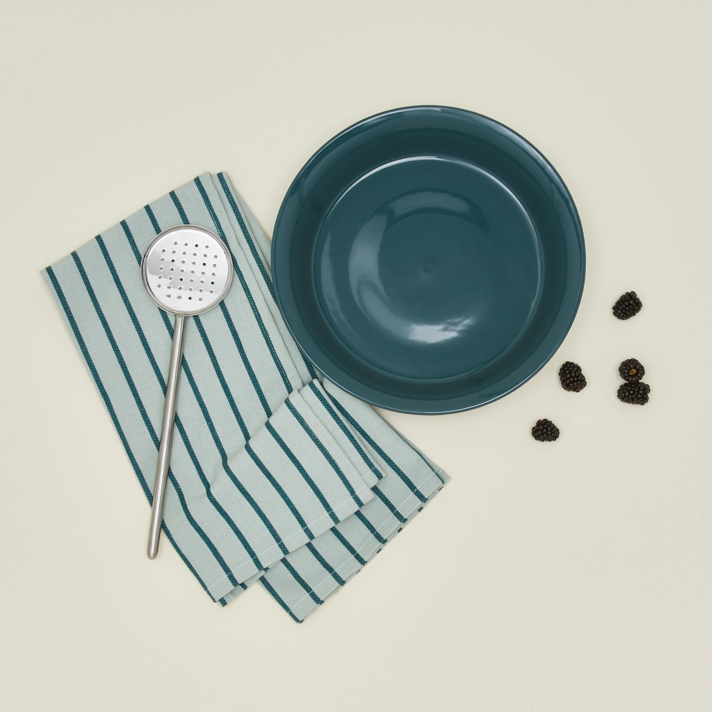 Essential pie dish in peacock with slotted spoon blackberries and dishtowel