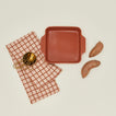 8" x 8" bakeware in terracotta with sweet potatoes, measuring spoons, and dish towel