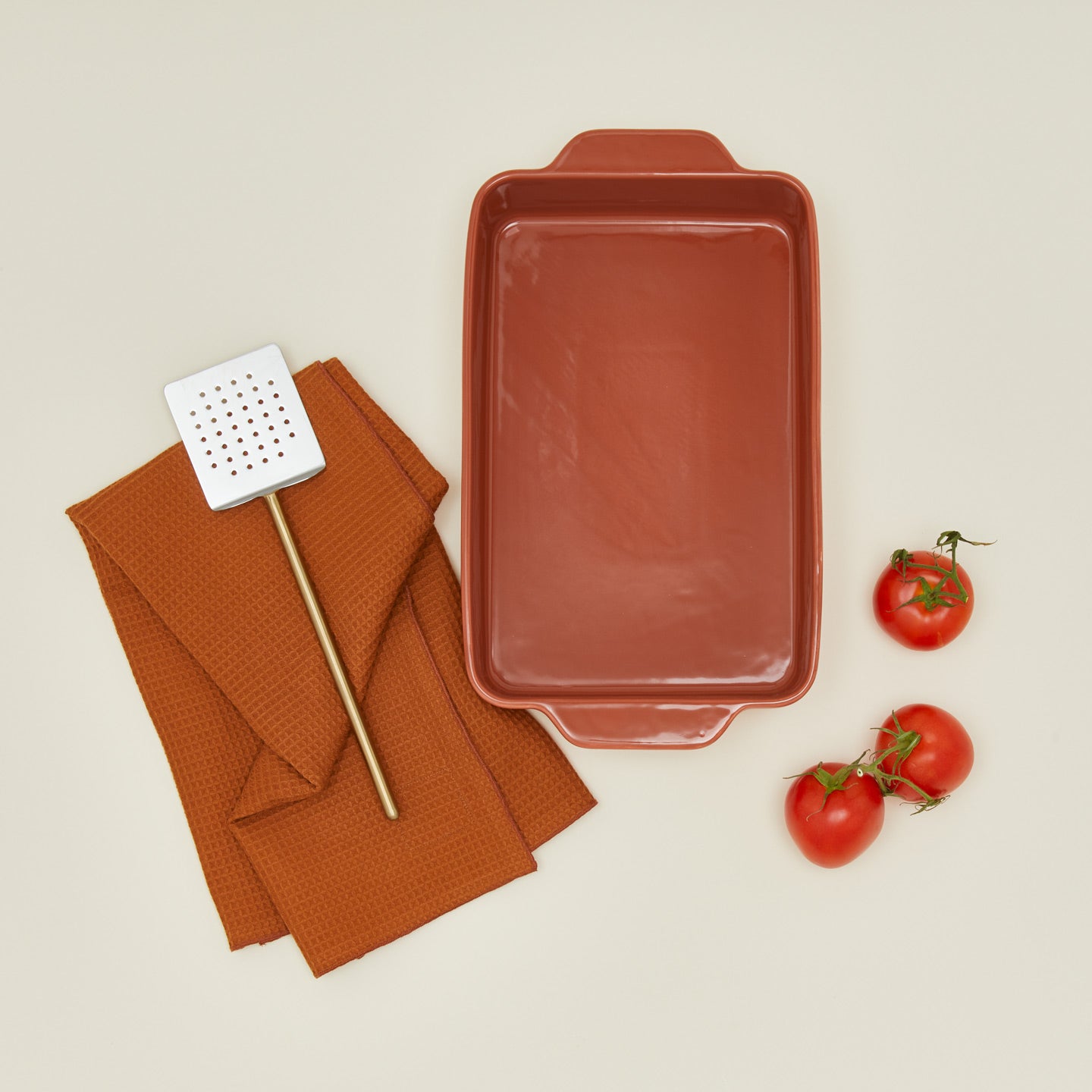 9x13 bakeware in terracotta with tomatoes dish towel and brass handled spatula
