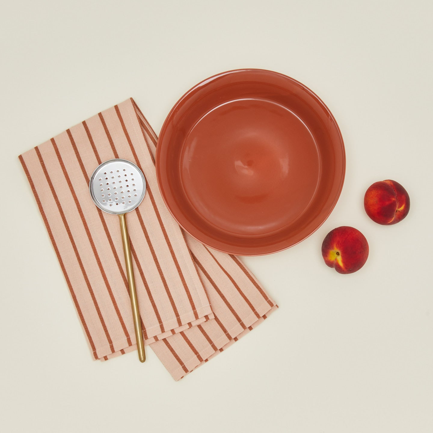 Essential pie dish in terracotta, with peaches, slotted spoon, and dish towel