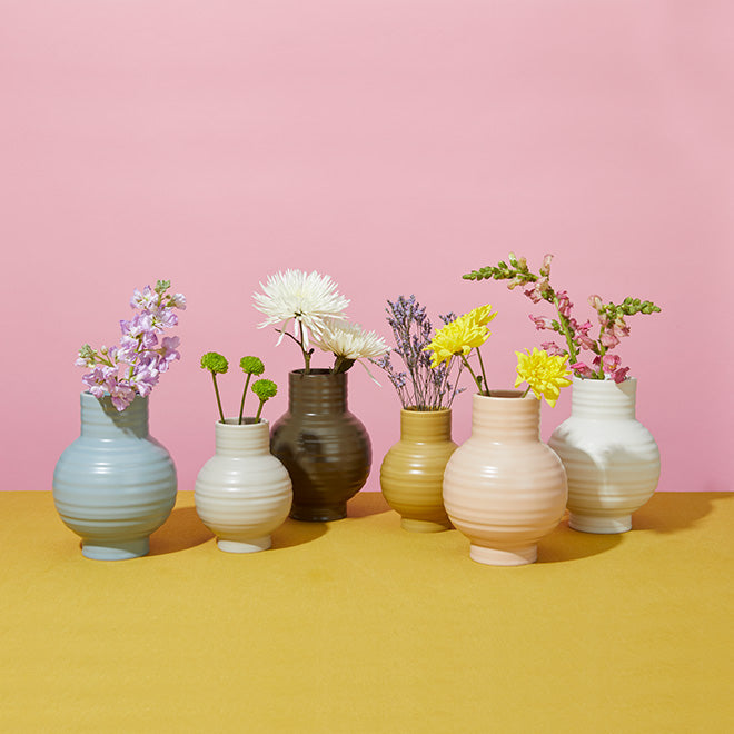 A group of six vases with flowers on a yellow tabletop.