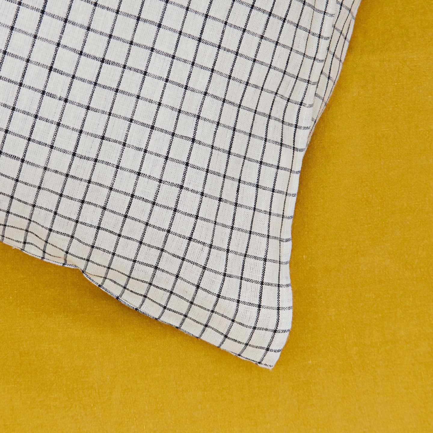 A close up of a checked linen pillow case on a mustard sheet.