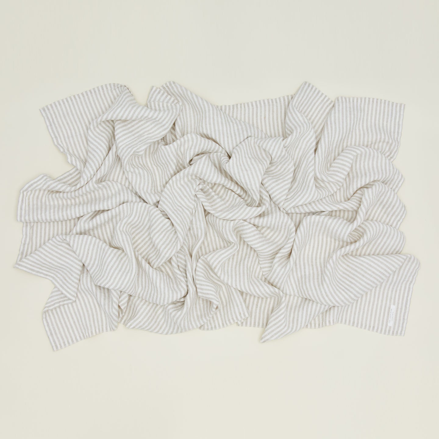 An overhead of a rumpled chambray linen throw with white stripes.