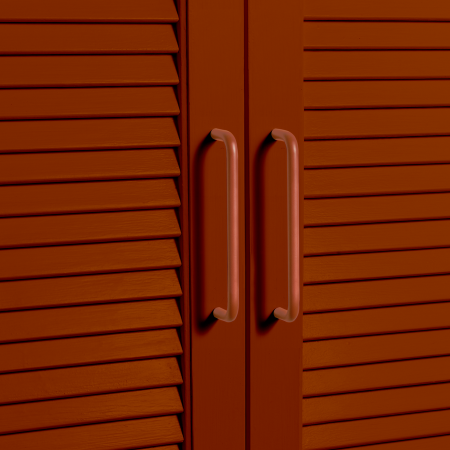 Close-up of a terracotta cabinet with horizontal slats and two terracotta colored handles.