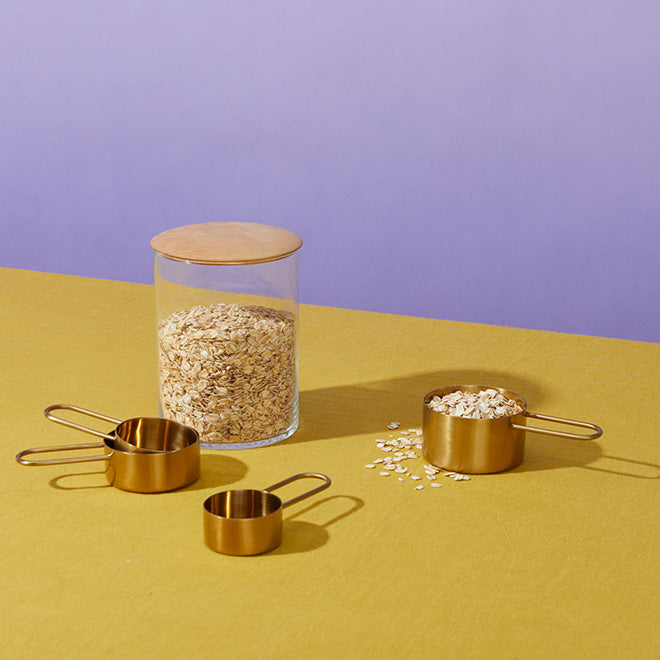 A kitchen storage canister and measuring cups full of rolled oats on a yellow tabletop.