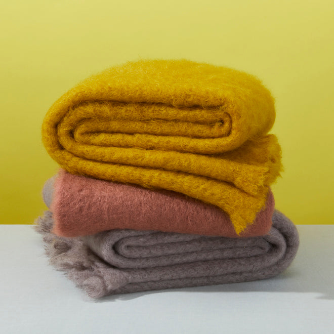 Stack of mohair throws in mustard, dark pink and grey. 