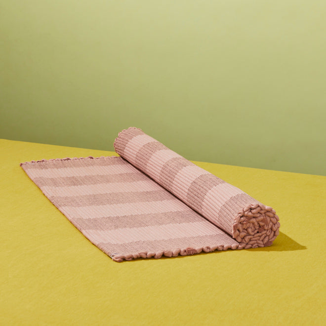 Essential mat in blush rolled on a yellow background.