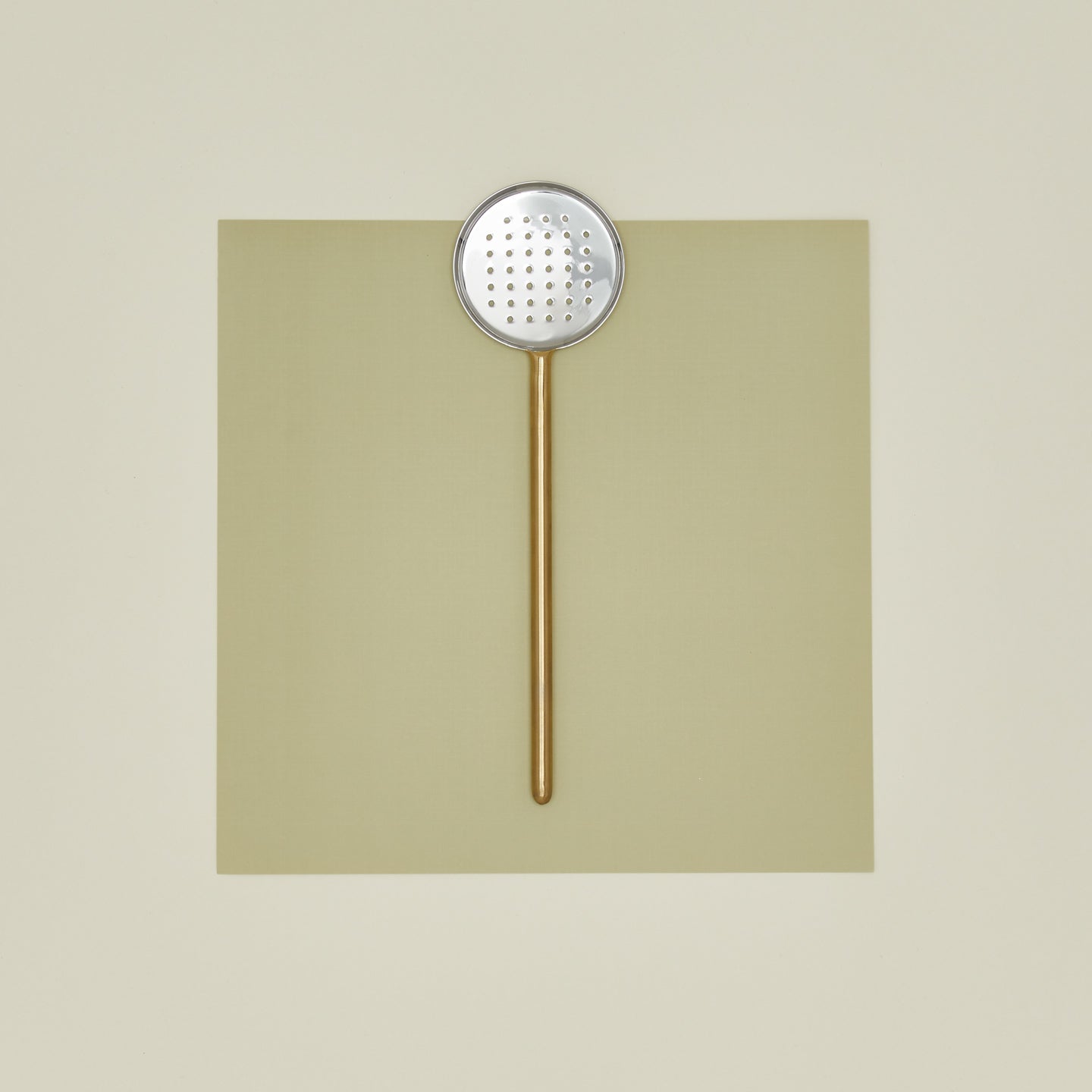 Simple metal flat slotted spoon in brass on colored paper.