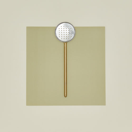 Simple metal flat slotted spoon in brass on colored paper.