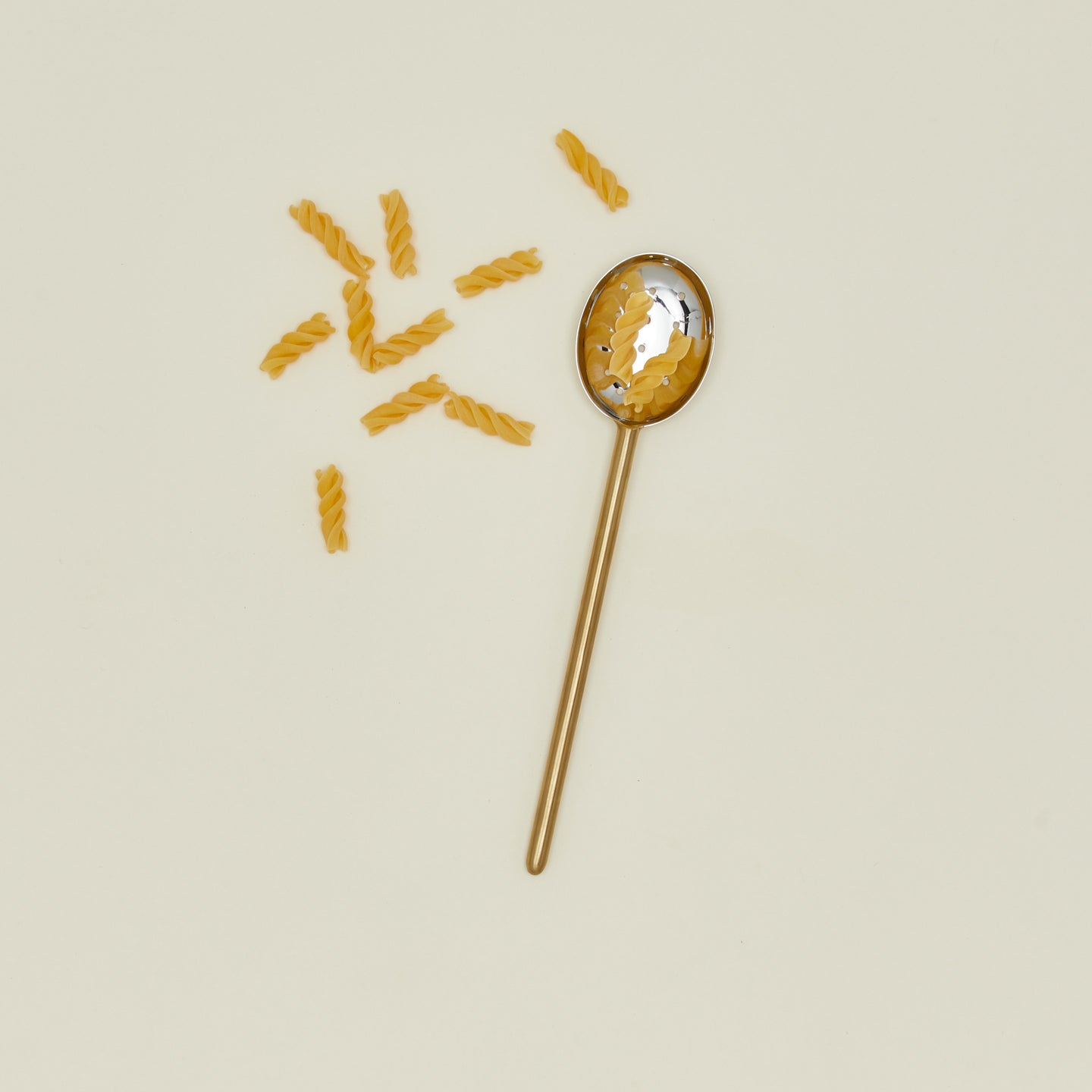 Simple metal slotted spoon in brass with pasta