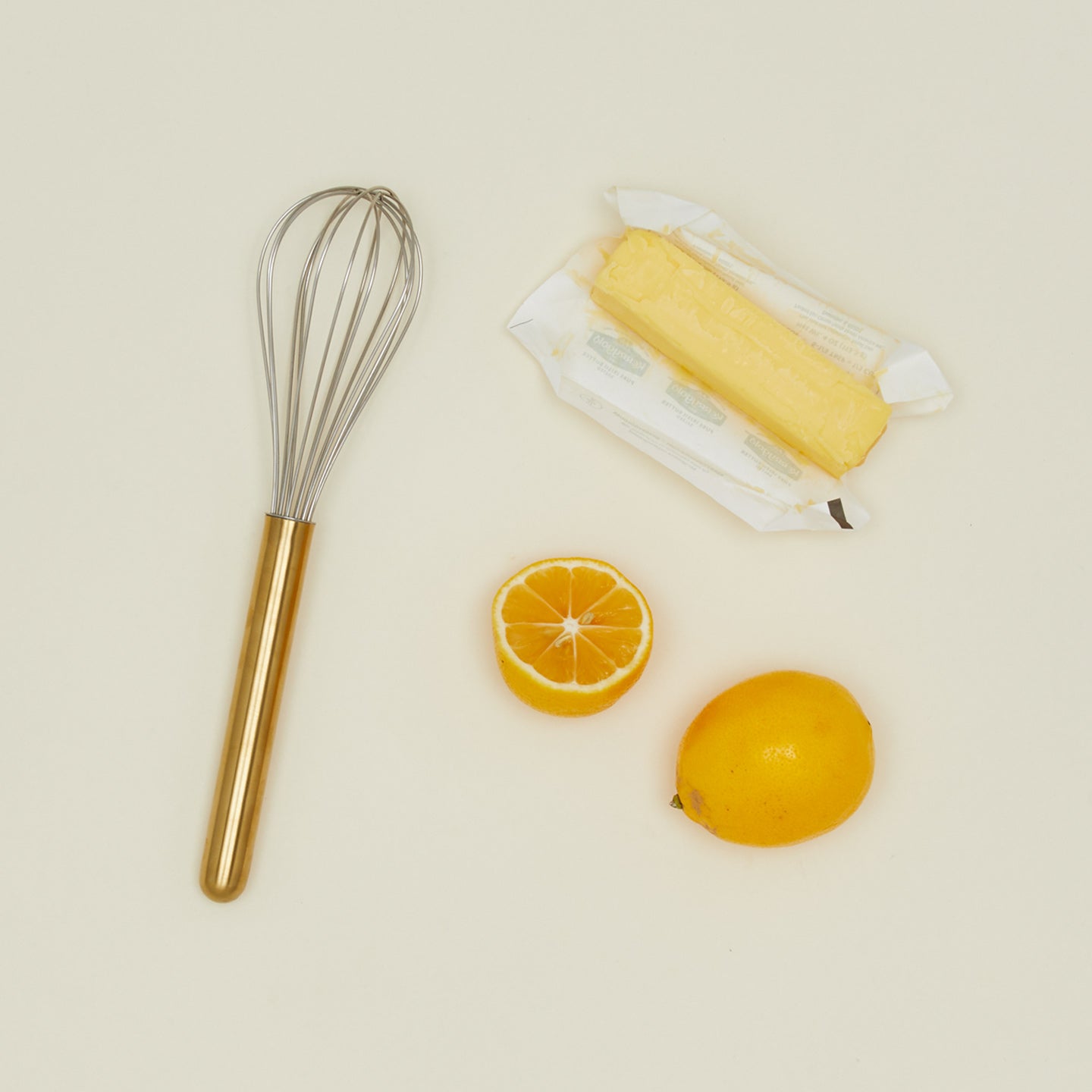 Simple metal whisk in brass with butter and oranges
