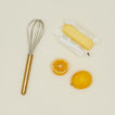 Simple metal whisk in brass with butter and oranges