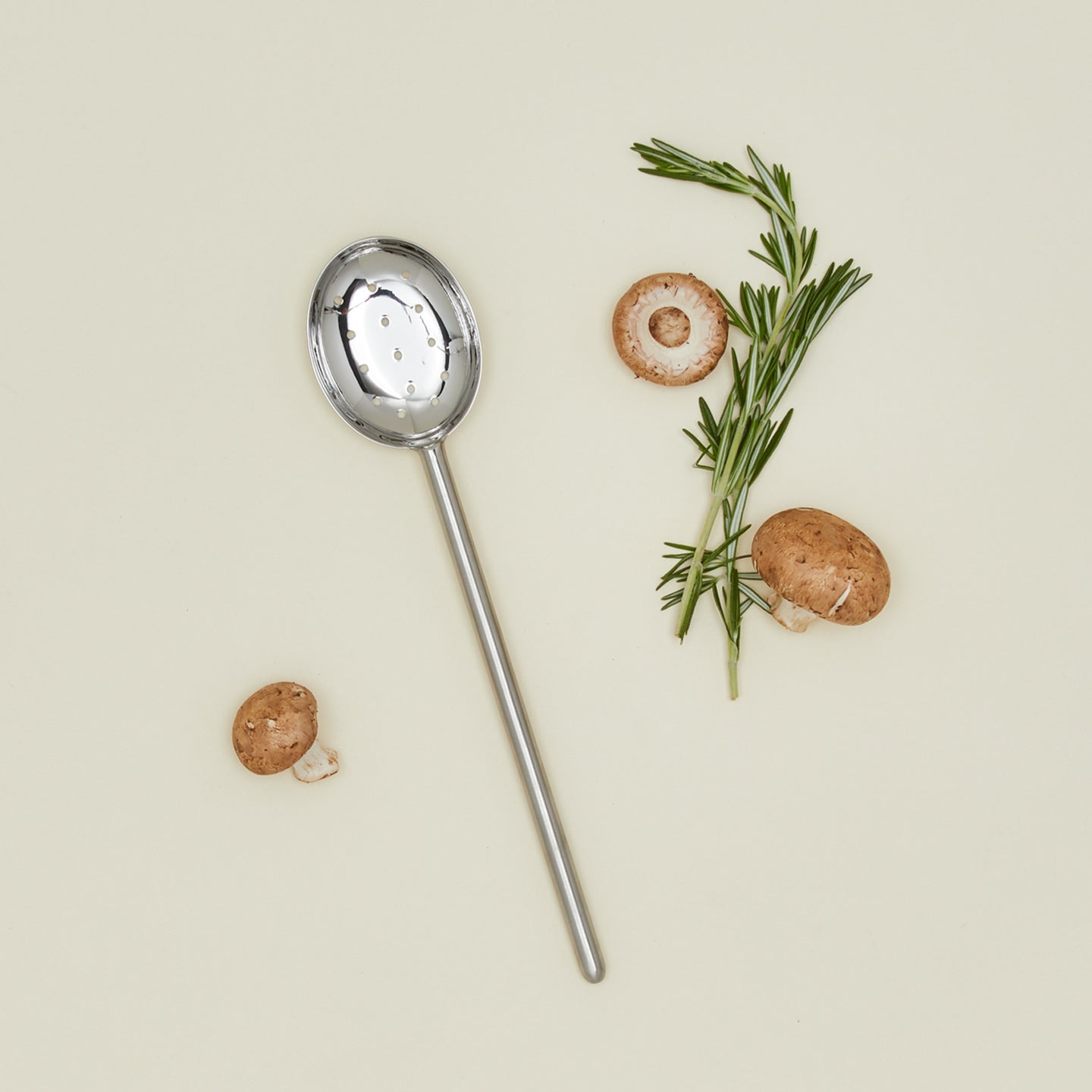 Simple metal slotted spoon in silver with rosemary and mushrooms
