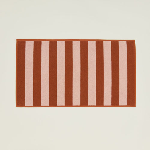 An overhead of a striped blush and terracotta terry bath mat.