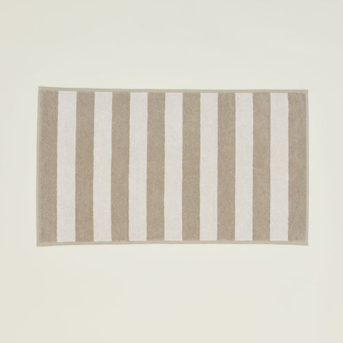 An overhead of a striped ivory and flax terry bath mat.