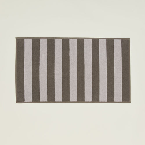 An overhead of a striped light grey and dark grey terry bath mat.