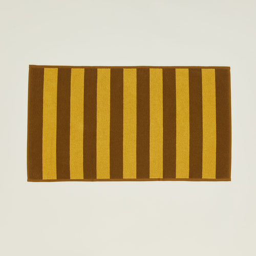 An overhead of a striped mustard and bronze terry bath mat.