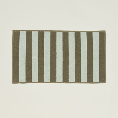 An overhead of a striped olive and sage terry bath mat.