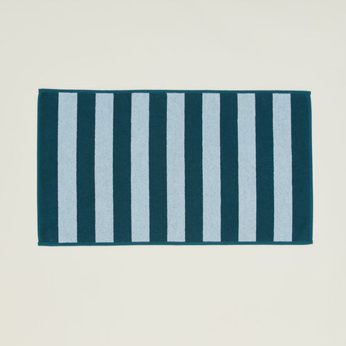 An overhead of a striped sky and peacock terry bath mat.