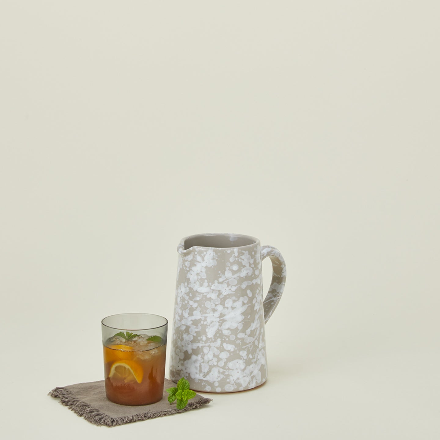 Small splatterware pitcher in grey and white with glass on a cocktail napkin