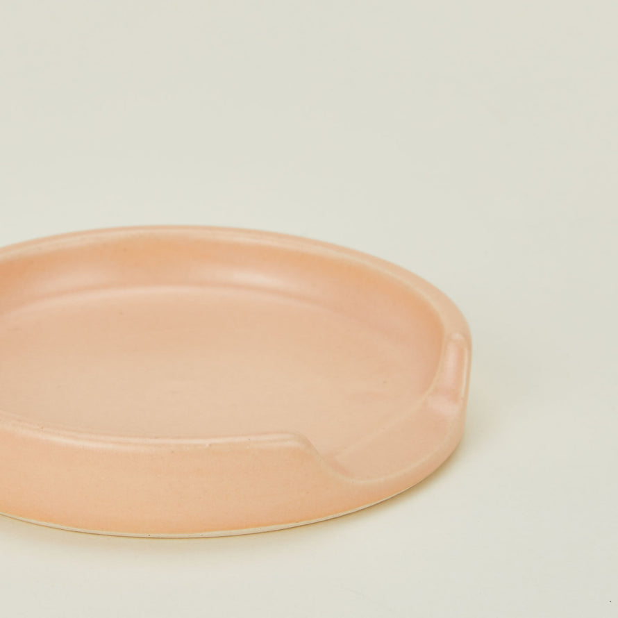 A close up of a blush stoneware spoon rest.