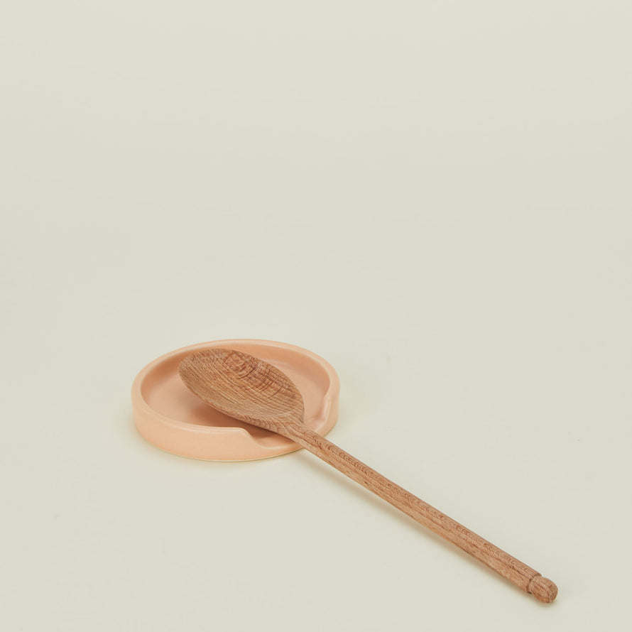 A blush stoneware spoon rest with a wooden spoon.