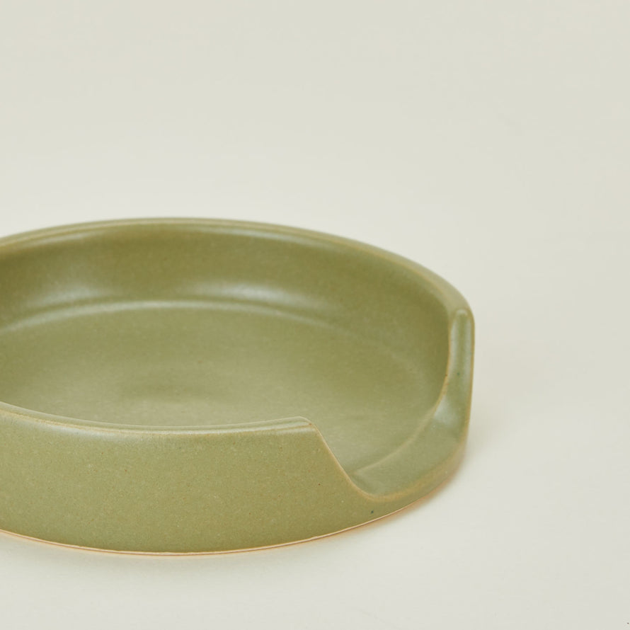 A close up of an olive stoneware spoon rest.