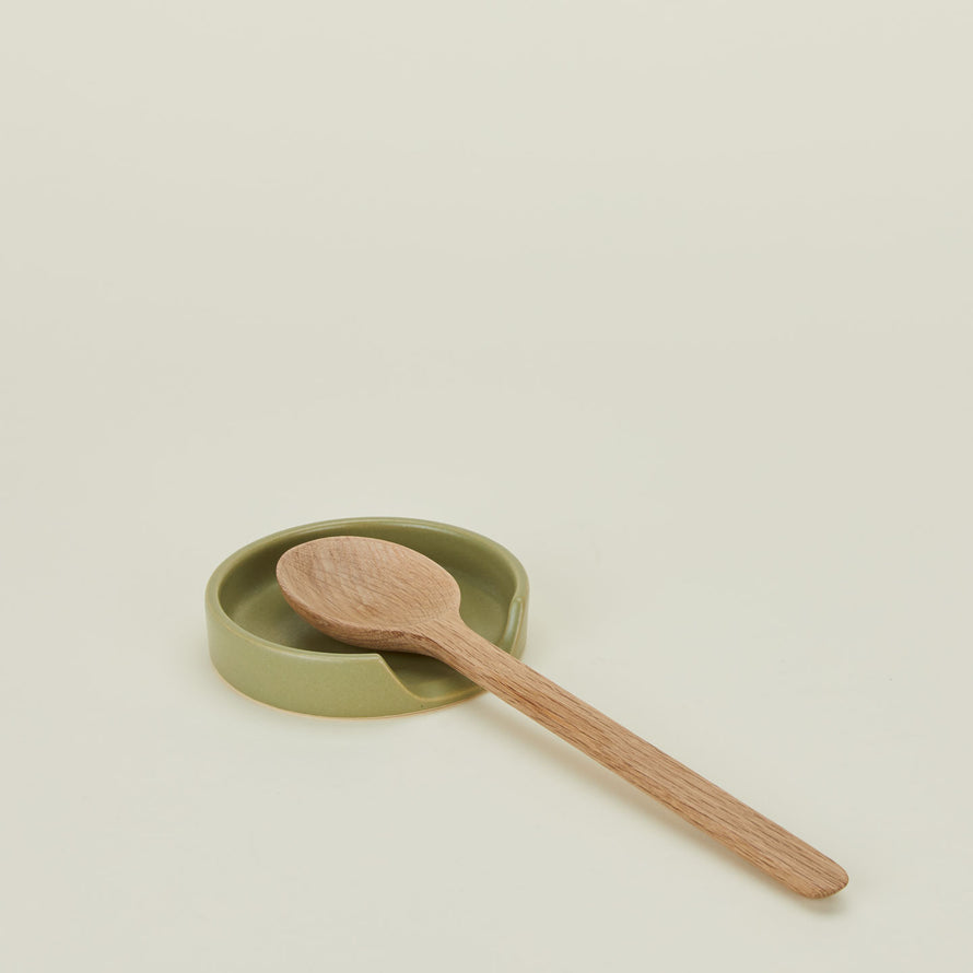 An olive stoneware spoon rest with a wooden spoon.