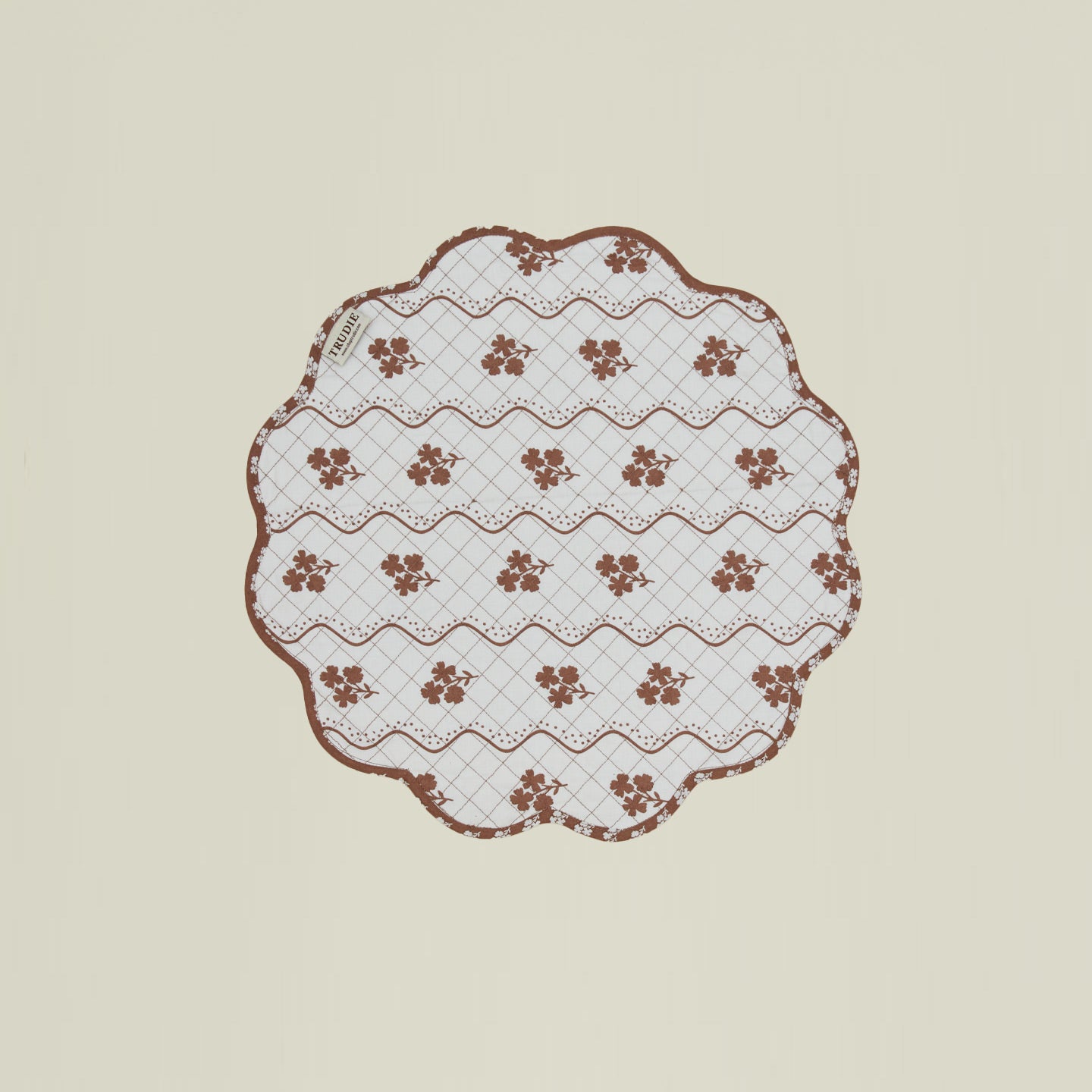 A round quilted placemat with a floral print in Constance brown.