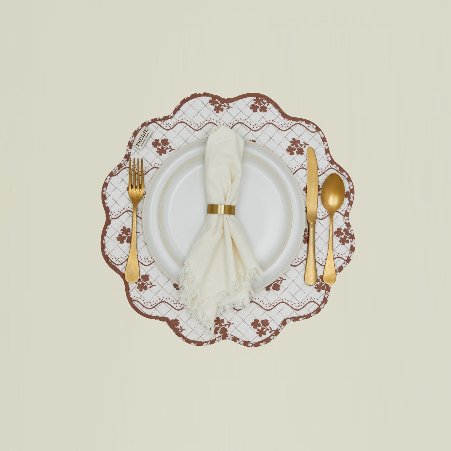 A place setting with a round quilted placemat with a floral print in Constance brown.
