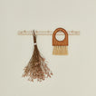 Wooden broom and bundle of dried florals hanging on a hook rack against a beige wall.