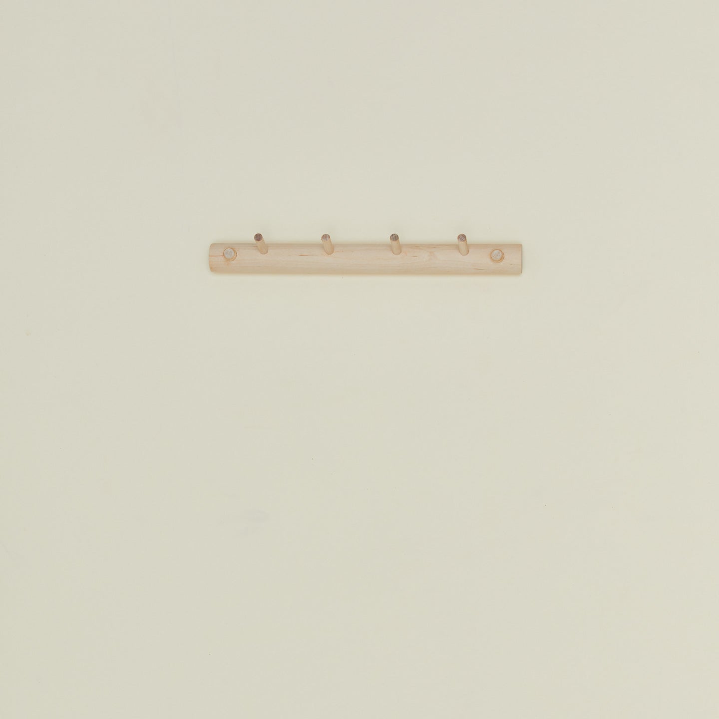 Small wooden coat rack with four hooks on a beige wall