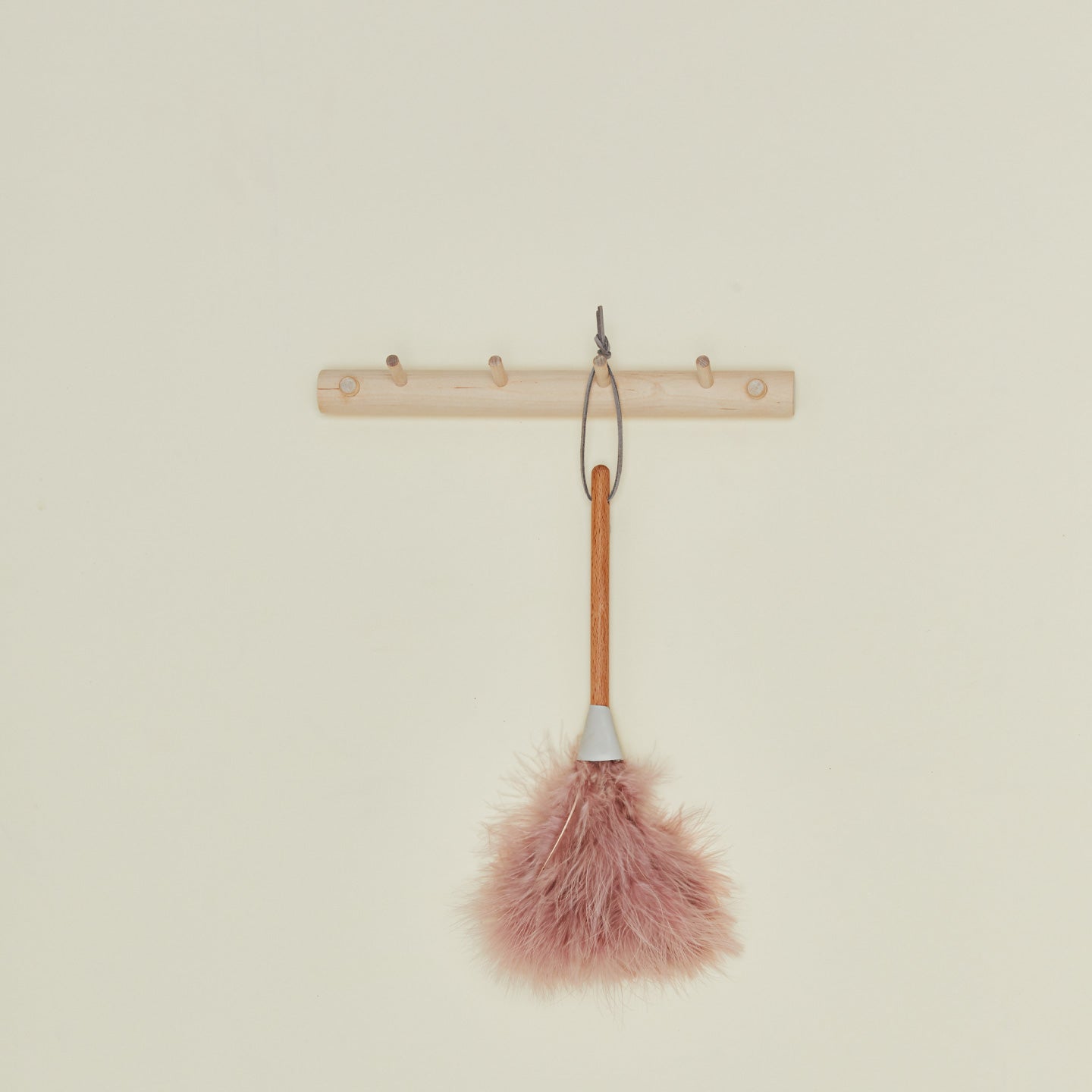Pink feather duster attached to a wooden hook on a beige background