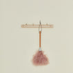 Pink feather duster attached to a wooden hook on a beige background